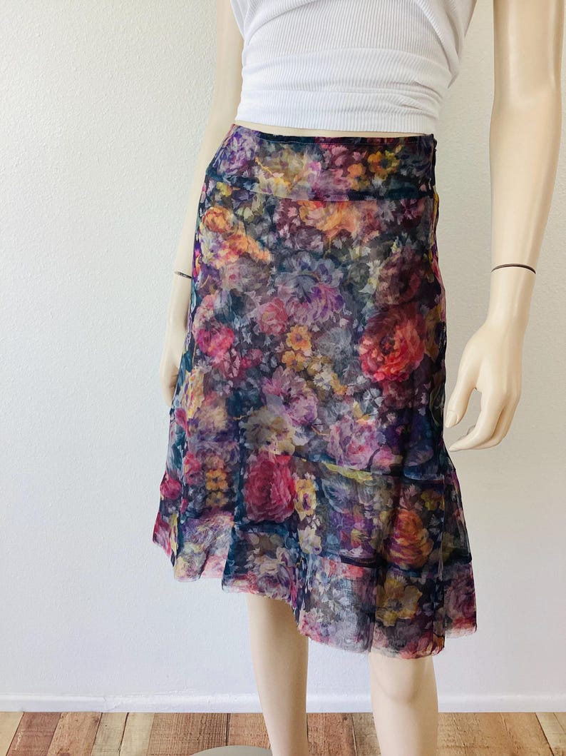 May include: A floral print skirt with a vibrant mix of pink, purple, yellow, and orange flowers on a dark background. The skirt has a layered, ruffled hemline and a flowing silhouette, suitable for a spring or summer outfit.