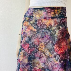 May include: A colourful floral print skirt in shades of pink, purple, yellow, and orange. The skirt has a flowing, layered design and is made of a sheer fabric. The skirt is part of a clothing collection.