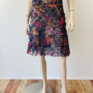 May include: A floral knee-length skirt with a layered design. The skirt has a dark blue base with a vibrant pattern of pink, red, and yellow flowers. The skirt is made of a sheer fabric.