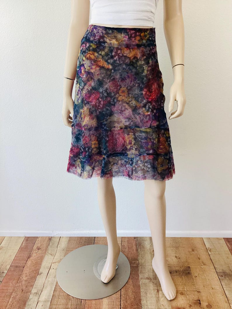 May include: A floral knee-length skirt with a layered design. The skirt has a dark blue base with a vibrant pattern of pink, red, and yellow flowers. The skirt is made of a sheer fabric.