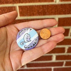 Puede incluir: Un bot&oacute;n morado y azul con rayas blancas y un gato de dibujos animados. El bot&oacute;n dice "GOOFY GOOBER" en texto blanco.