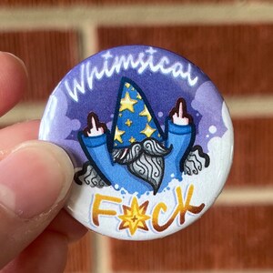 Puede incluir: Un botón redondo con un diseño de gnomo caprichoso. El gnomo lleva un sombrero de mago azul con estrellas doradas y una túnica azul. El botón tiene las palabras "Whimsical" y "F*ck" en letras doradas.