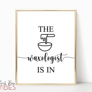 May include: A gold framed print with the text "The Waxologist is in" in black lettering. A black and white illustration of a bowl with wax dripping into it is above the text.
