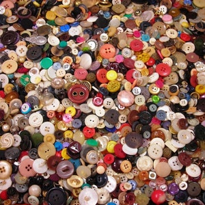 May include: A large assortment of buttons in various sizes, shapes, and colors. The buttons are made of different materials, including plastic, wood, and metal. Colors include red, white, black, brown, yellow, and green. The buttons are scattered, creating a textured surface.