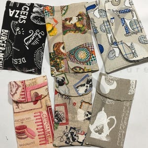 May include: Six different fabric pouches with various patterns. The pouches are made of a light brown fabric with different designs printed on them. The designs include a burger menu, cupcakes, dogs, and a teapot.