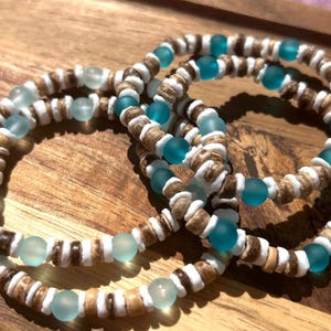 May include: Several beaded bracelets with a beachy theme. The bracelets feature a combination of light blue, white, and brown beads. The beads are strung together to create a unique and stylish accessory.