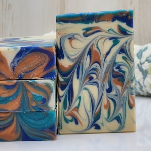 May include: Four bars of handmade soap stacked on top of each other. The soap is a swirl of blue, white, and brown colors. A single bar of soap is shown next to the stack.