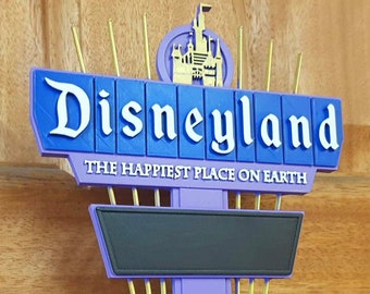 May include: A purple and blue Disneyland sign with the text "Disneyland" and "The Happiest Place on Earth".