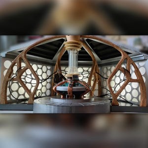 May include: A detailed model of the Doctor Who TARDIS console room, featuring a brown wooden frame, a circular control panel with a clear glass tube, and a figure of the Doctor standing in the room.