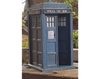 May include: A blue and black miniature replica of a classic British police telephone box. The box has a sign that reads "Police Public Call Box" and a smaller sign that reads "Free and for Public Use - Pull to Open".