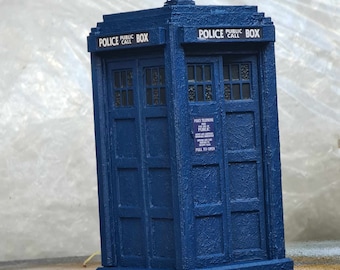 May include: A blue painted model of a classic British police telephone box with the text "Police Public Call" on the top. The box has a door with a sign that reads "Police Telephone Free To The Public" and "Pull To Open".