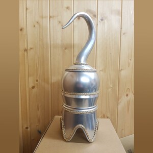 以下が含まれることがあります： 海賊の鉤爪に似た、湾曲した刃を持つ銀色の装飾用フック。 フックは3層のベースに取り付けられており、各層の周りに金色のロープのディテールがあります。 フックは木製の背景に対して段ボール箱に表示されています。