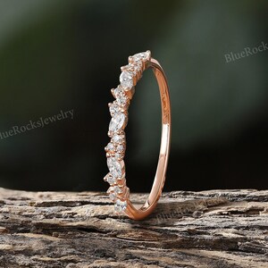 May include: A delicate rose gold band with a row of small, sparkling diamonds set in a marquise shape. The band is thin and simple, making it a perfect choice for a wedding band or an everyday ring.