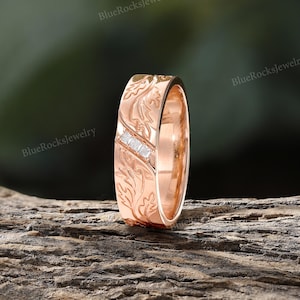 Pode incluir: Um anel de ouro rosa com um padr&atilde;o de folhas em relevo na superf&iacute;cie e um canal diagonal cravejado com tr&ecirc;s pequenas pedras transparentes de corte quadrado. O metal tem um acabamento polido e um motivo bot&acirc;nico cont&iacute;nuo.