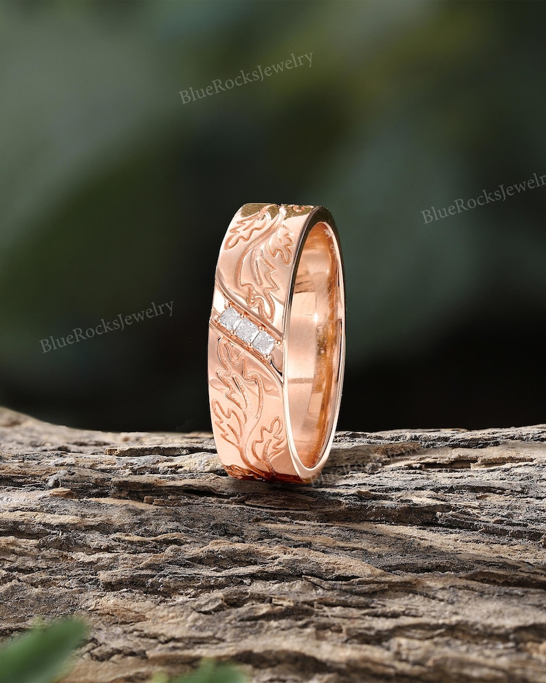 Pode incluir: Um anel de ouro rosa com um padr&atilde;o de folhas em relevo na superf&iacute;cie e um canal diagonal cravejado com tr&ecirc;s pequenas pedras transparentes de corte quadrado. O metal tem um acabamento polido e um motivo bot&acirc;nico cont&iacute;nuo.