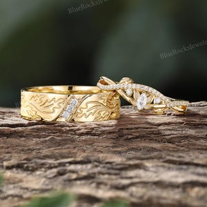 Pode incluir: Uma alian&ccedil;a de ouro com um padr&atilde;o de folhas gravado e tr&ecirc;s pequenos diamantes quadrados, combinada com um anel de ouro a condizer com um diamante central em corte marquise, diamantes redondos mais pequenos e um design de banda torcida.