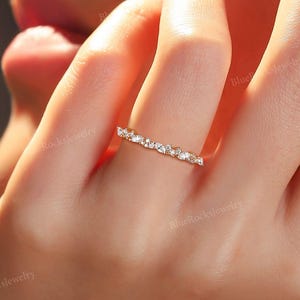 May include: A delicate gold band ring with a row of small, clear, round and oval-shaped stones.