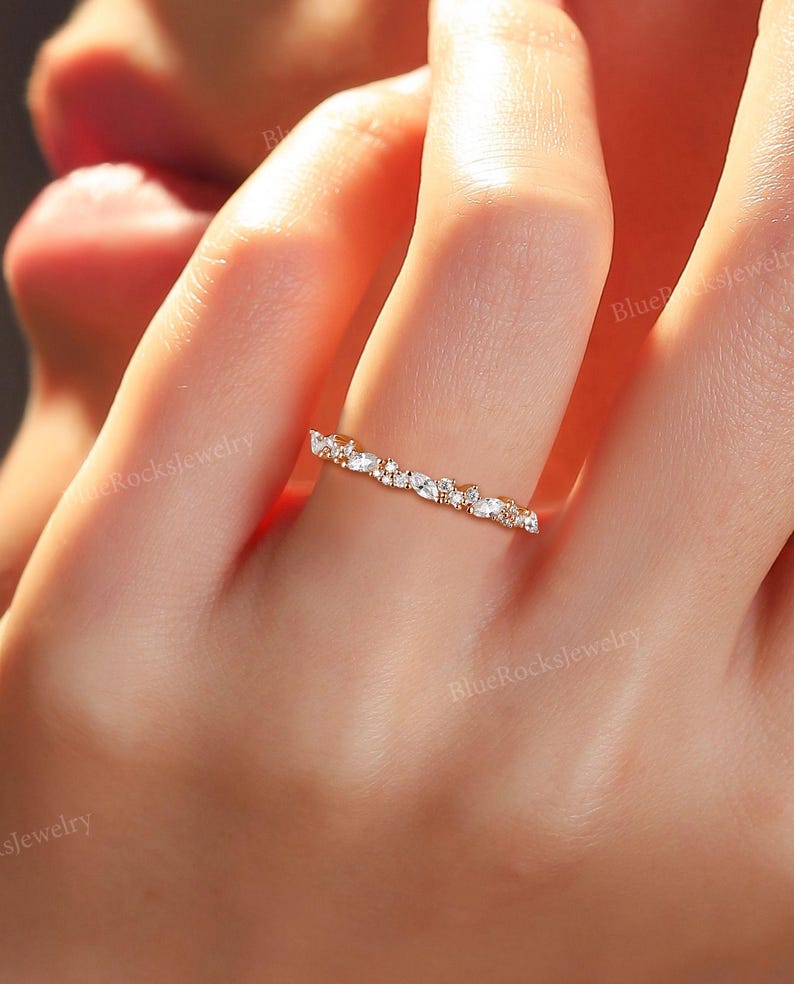 May include: A delicate gold band ring with a row of small, clear, round and oval-shaped stones.