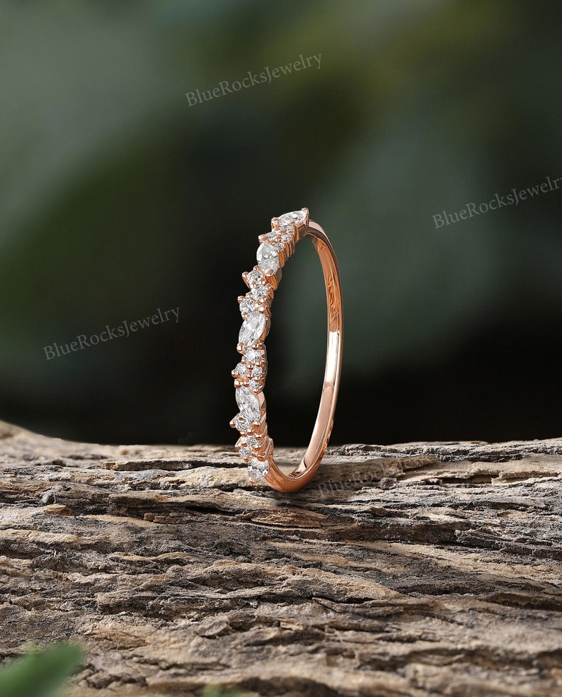 May include: A delicate rose gold band with a row of small, sparkling diamonds set in a marquise shape. The band is thin and simple, making it a perfect choice for a wedding band or an everyday ring.