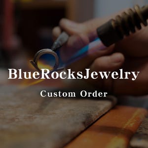May include: A close-up of a metal ring being heated with a torch. The ring is glowing orange and the torch is producing a blue flame. The text "BlueRocks.Jewelry Custom Order" is visible below the ring.