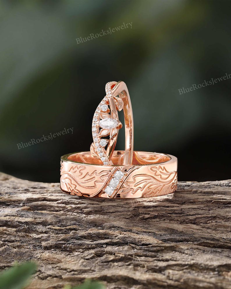 Pode incluir: Um conjunto de an&eacute;is em ouro rosa composto por uma alian&ccedil;a com padr&atilde;o de folhas gravado e tr&ecirc;s pequenas pedras quadradas, e uma alian&ccedil;a curva com uma pedra central de corte marquise rodeada por pequenas pedras redondas e detalhes de folhas.