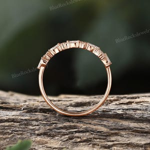 May include: A delicate rose gold band with a row of small, clear, baguette-shaped stones set in a prong setting.