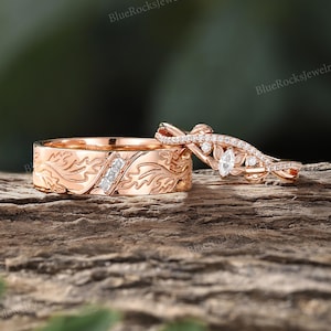 Pode incluir: Uma alian&ccedil;a de ouro rosa com um padr&atilde;o de folhas gravado e tr&ecirc;s pequenos diamantes quadrados, combinada com um anel de ouro rosa a condizer com um diamante central em talhe marquise, pedras redondas pequenas e uma banda torcida.