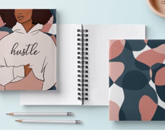 May include: Two spiral bound notebooks. The front cover of one notebook features a black and white illustration of a person wearing a hoodie with the word "hustle" printed on it. The background is a pink and white abstract pattern. The front cover of the other notebook features a pink, white, and blue abstract pattern.