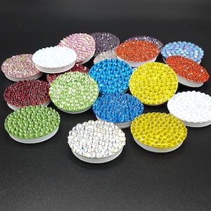 May include: Assortment of colorful phone grips with rhinestone embellishments. The grips are round and come in various colors, including red, green, blue, yellow, and white.