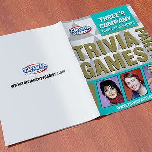 Puede incluir: Un libro azul y dorado con el t&iacute;tulo "Three's Company Trivia Showdown Trivia Games Party" e im&aacute;genes de los tres personajes principales del programa.