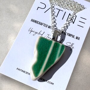 May include: A silver chain necklace with a green and white ceramic pendant. The pendant is shaped like a jagged piece of rock. The necklace is handmade and comes with a tag that says "PATINE Jewelry by Sally".