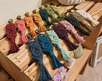 May include: A collection of colorful macrame keychains with tassels. The keychains are made with different colored cords and feature a variety of knot patterns.
