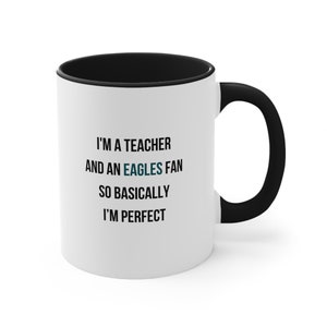 May include: White ceramic coffee mug with a black rim and handle. The mug has black text that reads "I'm a teacher and an Eagles fan so basically I'm perfect."