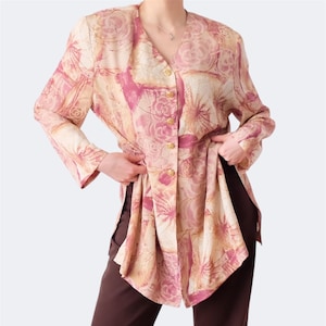 Puede incluir: Blusa vintage con estampado floral en tonos rosa, beige y blanco, con botones dorados. La parte superior de manga larga se combina con pantalones marrones oscuros. La blusa tiene cuello en V.