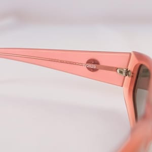 Pode incluir: Close-up de &oacute;culos de sol cor-de-rosa. A arma&ccedil;&atilde;o &eacute; de cor s&oacute;lida e transl&uacute;cida. A dobradi&ccedil;a e a haste s&atilde;o vis&iacute;veis, com o texto "W2529" impresso na haste. As lentes s&atilde;o de cor escura.