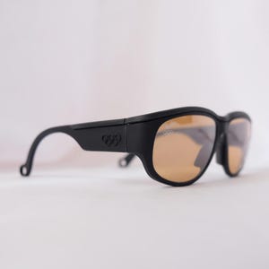 May include: Black sunglasses with brown lenses and the Olympic rings logo on the side.