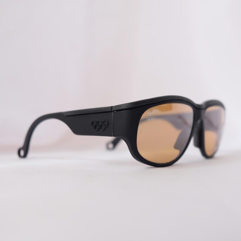 May include: Black sunglasses with brown lenses and the Olympic rings logo on the side.