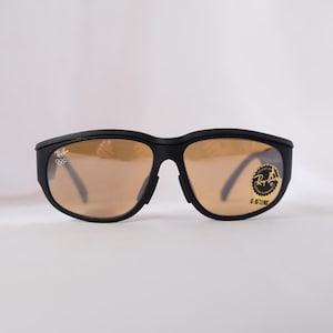 May include: Black wraparound sunglasses with brown lenses. The sunglasses have a Ray-Ban logo on the right lens and the text "G-15 LENS" on the right temple.