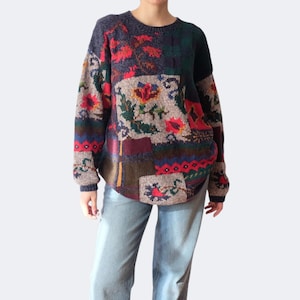 Op de afbeelding: Een vintage patchwork trui met een ronde hals. De trui heeft een mix van bloemen- en geometrische patronen in tinten rood, groen, bruin en blauw. De mouwen en zoom hebben een geribbeld ontwerp.
