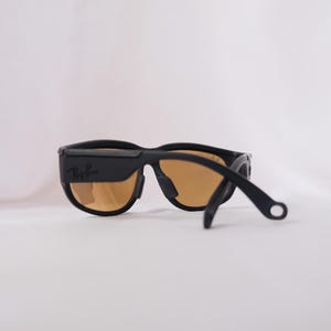 May include: Black Ray-Ban sunglasses with brown lenses and a black adjustable strap. The sunglasses have a sleek, modern design.
