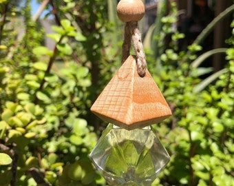May include: A wooden pyramid-shaped car air freshener with a clear glass bottle filled with a green liquid. The air freshener is hanging from a string with a wooden bead.