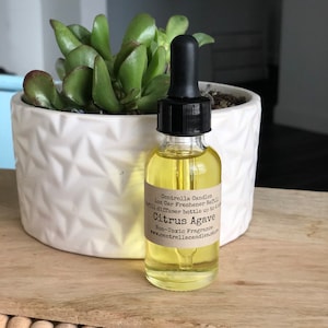 May include: A clear glass bottle with a black dropper top filled with a yellow liquid. The bottle has a brown label with the text "Centrella Candles 1oz Car Freshener Refill Citrus Agave Non-Toxic Fragrance www.centrellacandles.store diffuser bottle up to 4 oz".
