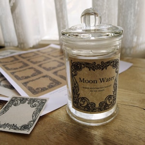 Può includere: Un barattolo di vetro trasparente con un coperchio di vetro e un'etichetta che recita "Moon Water cleanse and empower yourself for the month".