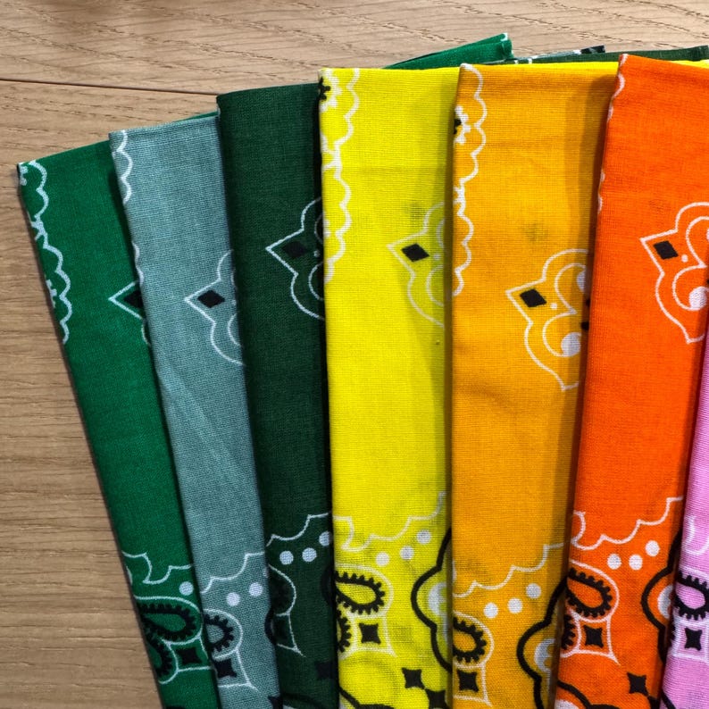 Puede incluir: Una colecci&oacute;n de pa&ntilde;uelos bandanas coloridos en tonos verdes, azules, amarillos, naranjas y rosas. Cada bandana presenta un dise&ntilde;o de cachemira blanco en los bordes y en el centro. Los pa&ntilde;uelos est&aacute;n doblados y dispuestos en forma de abanico.