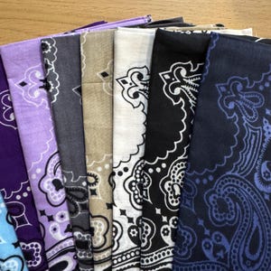 Puede incluir: Una colecci&oacute;n de pa&ntilde;uelos plegados en varios colores, incluyendo morado, gris, beige, blanco, negro y azul marino. Cada pa&ntilde;uelo presenta un dise&ntilde;o de cachemira en colores contrastantes, un accesorio cl&aacute;sico y vers&aacute;til.