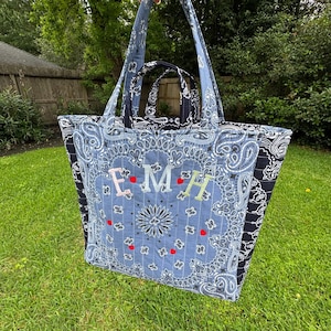 Puede incluir: Un bolso tote acolchado grande con un estampado de cachemira azul claro y las letras bordadas "EMH". El bolso tiene un bolso m&aacute;s peque&ntilde;o a juego en el interior y un estampado de cachemira negro en los laterales. El bolso tiene correas largas.