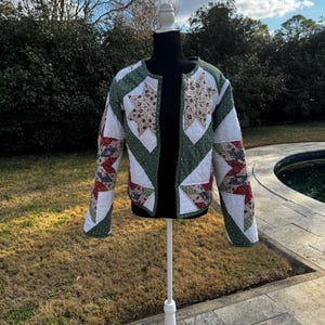 May include: A quilted jacket with a patchwork design. The jacket features a white base with green polka dot and star-shaped accents. The sleeves have red and patterned fabric. The jacket is displayed on a white mannequin.