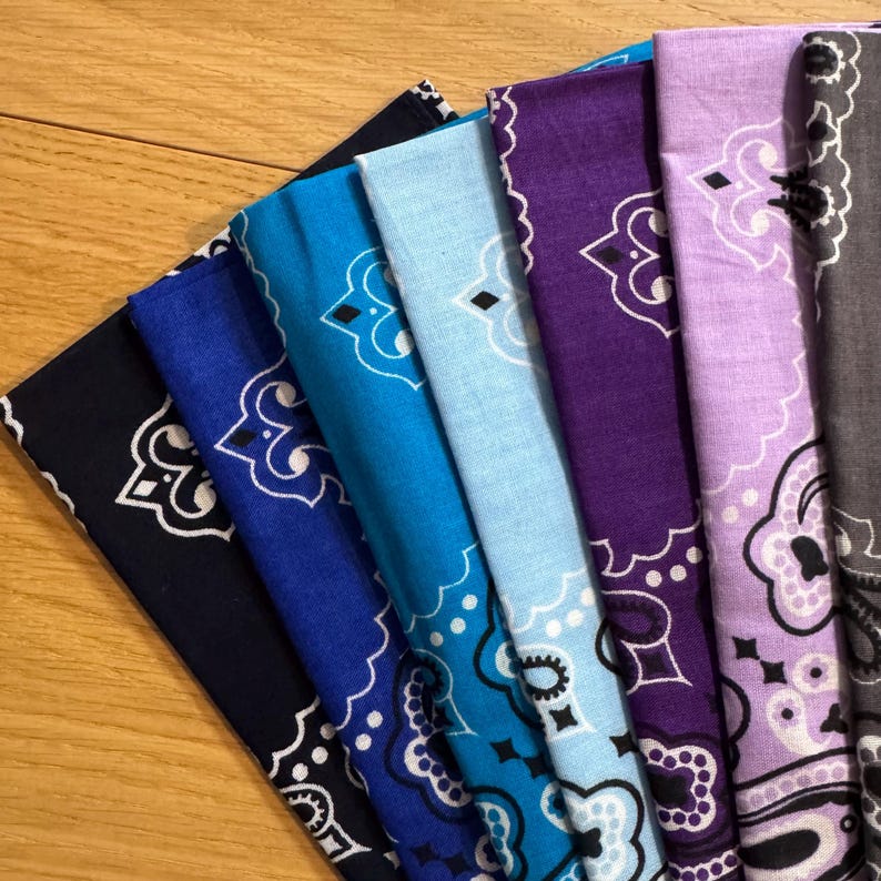 Puede incluir: Una colecci&oacute;n de pa&ntilde;uelos bandana en varios tonos de azul, morado y gris, cada uno con un dise&ntilde;o de cachemira blanco. Los pa&ntilde;uelos est&aacute;n cuidadosamente dispuestos, mostrando sus diferentes colores y patrones.