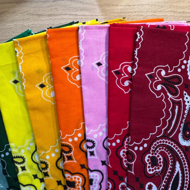 Puede incluir: Una colecci&oacute;n de pa&ntilde;uelos coloridos en tonos verdes, amarillos, naranjas, rosas y rojos. Cada pa&ntilde;uelo presenta un dise&ntilde;o de cachemira blanco. Los pa&ntilde;uelos est&aacute;n doblados y apilados, mostrando sus colores y patrones vibrantes.