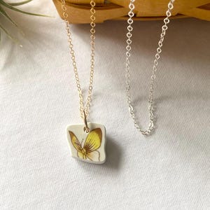 May include: A gold chain necklace with a porcelain pendant featuring a yellow butterfly. The pendant is attached to the chain with a gold jump ring.